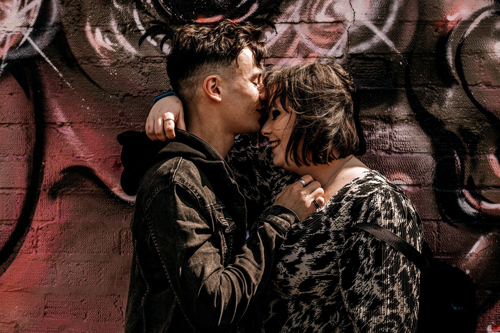 Intimate couple moment captured against urban wall art with dramatic lighting and shadows.