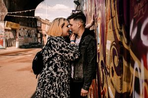 A couple shares an intimate moment against a graffiti wall at sunset on an urban street.