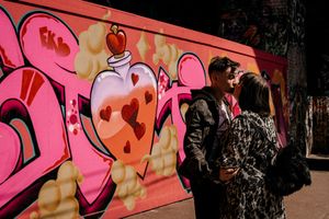 Two people stand by a vibrant pink street art mural featuring a heart design in an urban setting.