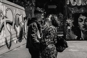 A black and white urban street scene with two figures in front of a wall covered in graffiti artwork.