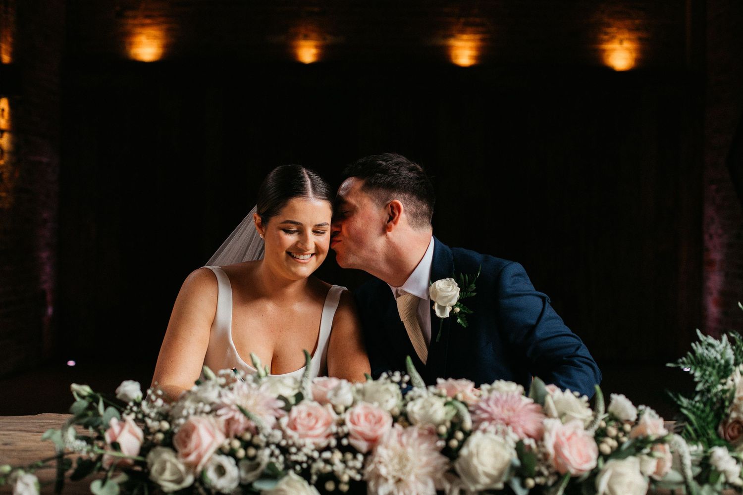 Wedding guests celebrate during a reception in a rustic brick venue with lattice wall decor and greenery.