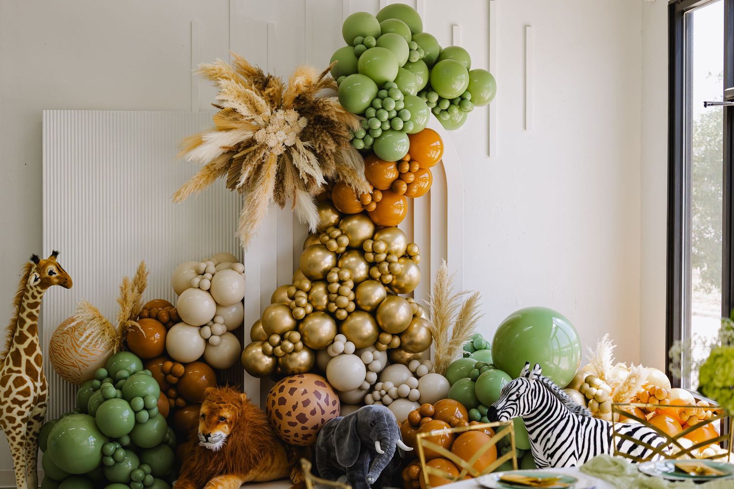 Luxurious safari-themed balloon arch installation with gold, green, and neutral colors featuring whimsical animal decorations.