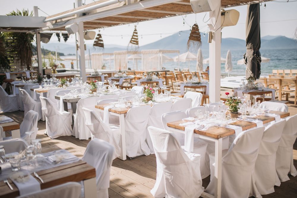 Elegant beachfront wedding reception setup with white chairs, coastal decor and mountain views in the background.