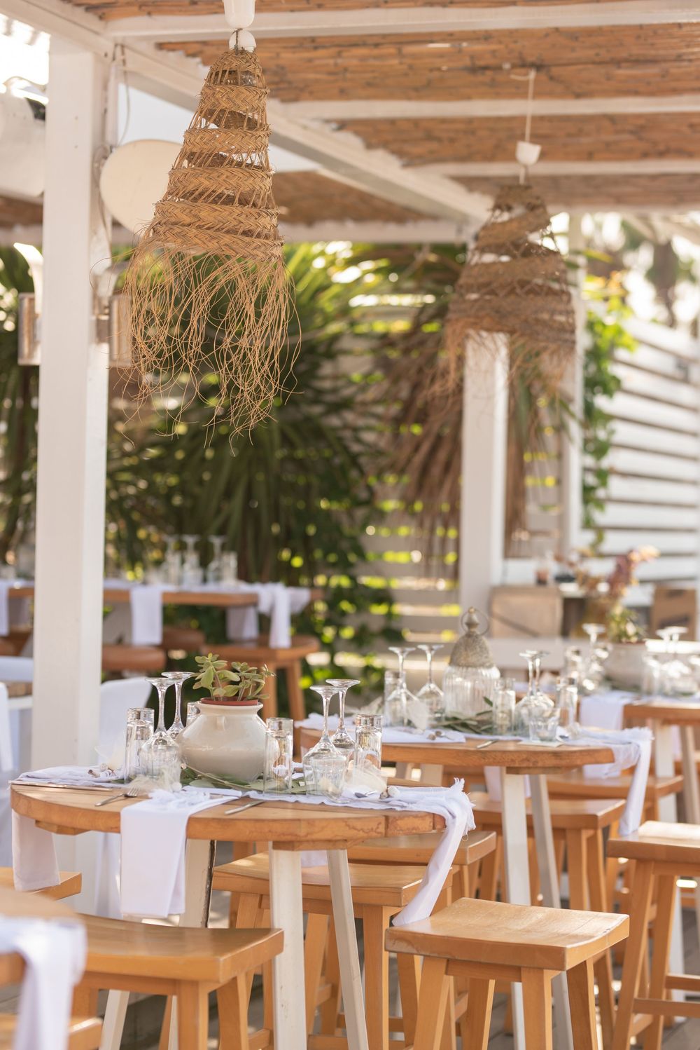 Rustic outdoor restaurant seating with natural woven pendant lights and wooden furniture under a covered patio.