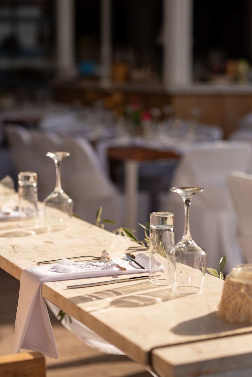 Table setting in a restaurant with upside-down wine glasses, white tablecloth, and soft natural lighting.