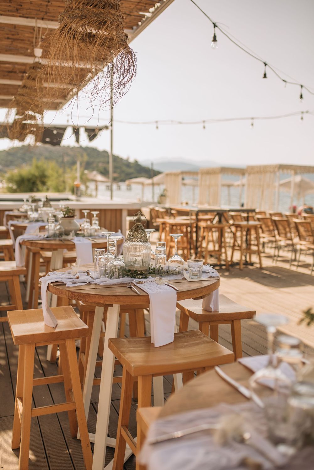 Rustic outdoor restaurant terrace with wooden tables and string lights overlooking mountain views at sunset.