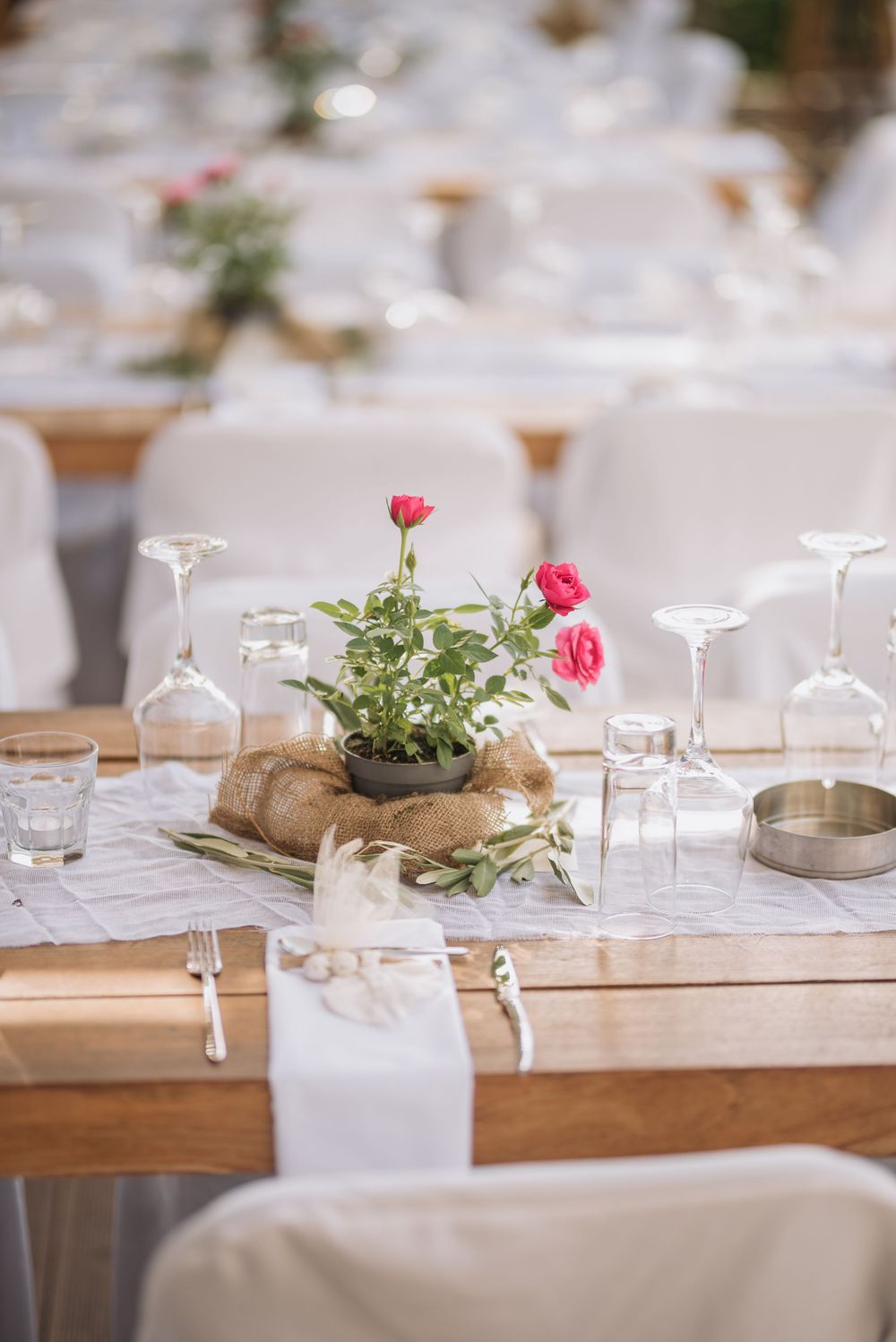 Elegant wedding table setting with pink flowers in burlap centerpiece and wine glasses on wooden table with white linens.
