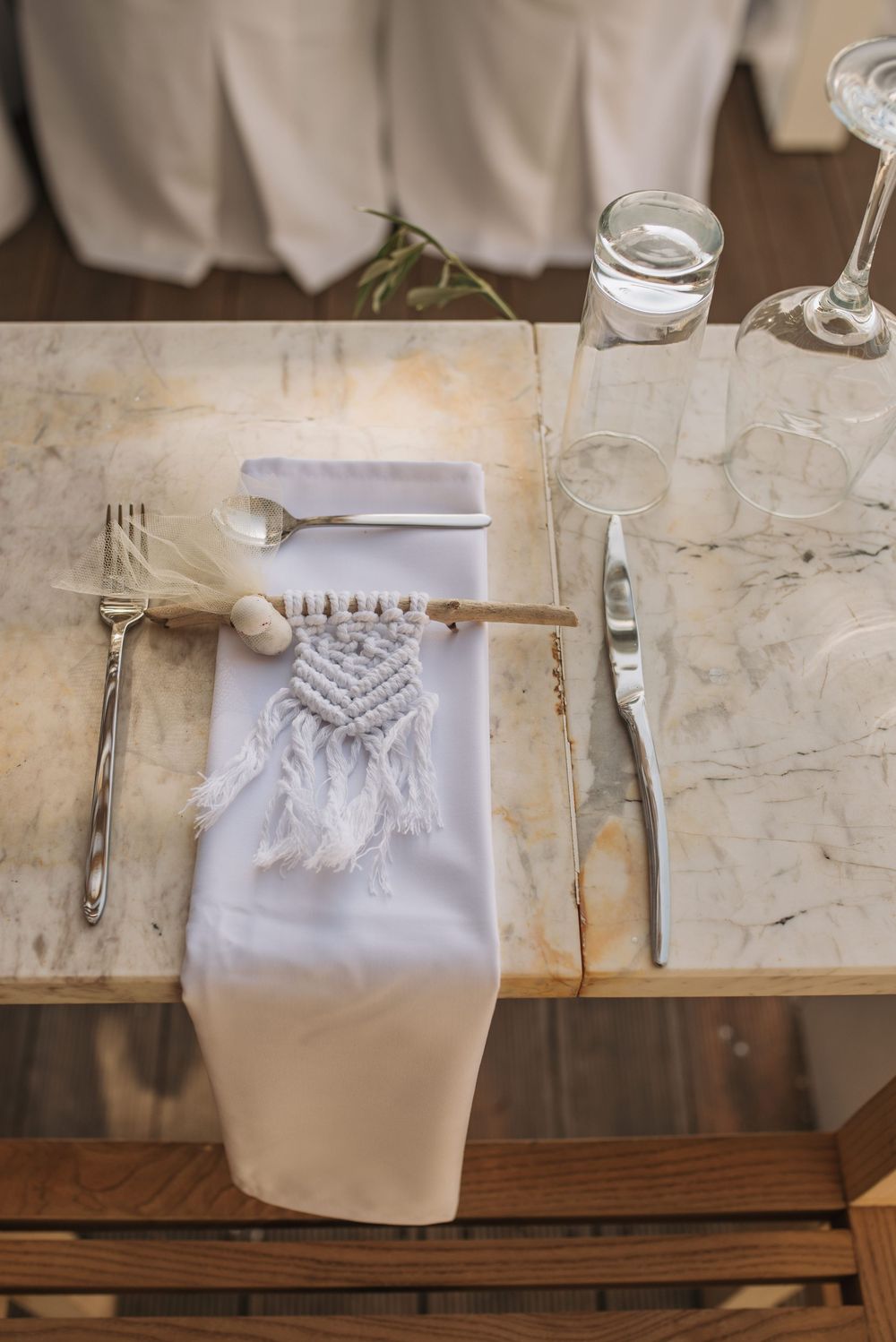 Elegant place setting with macrame napkin holder, glassware, and silverware on marble table.