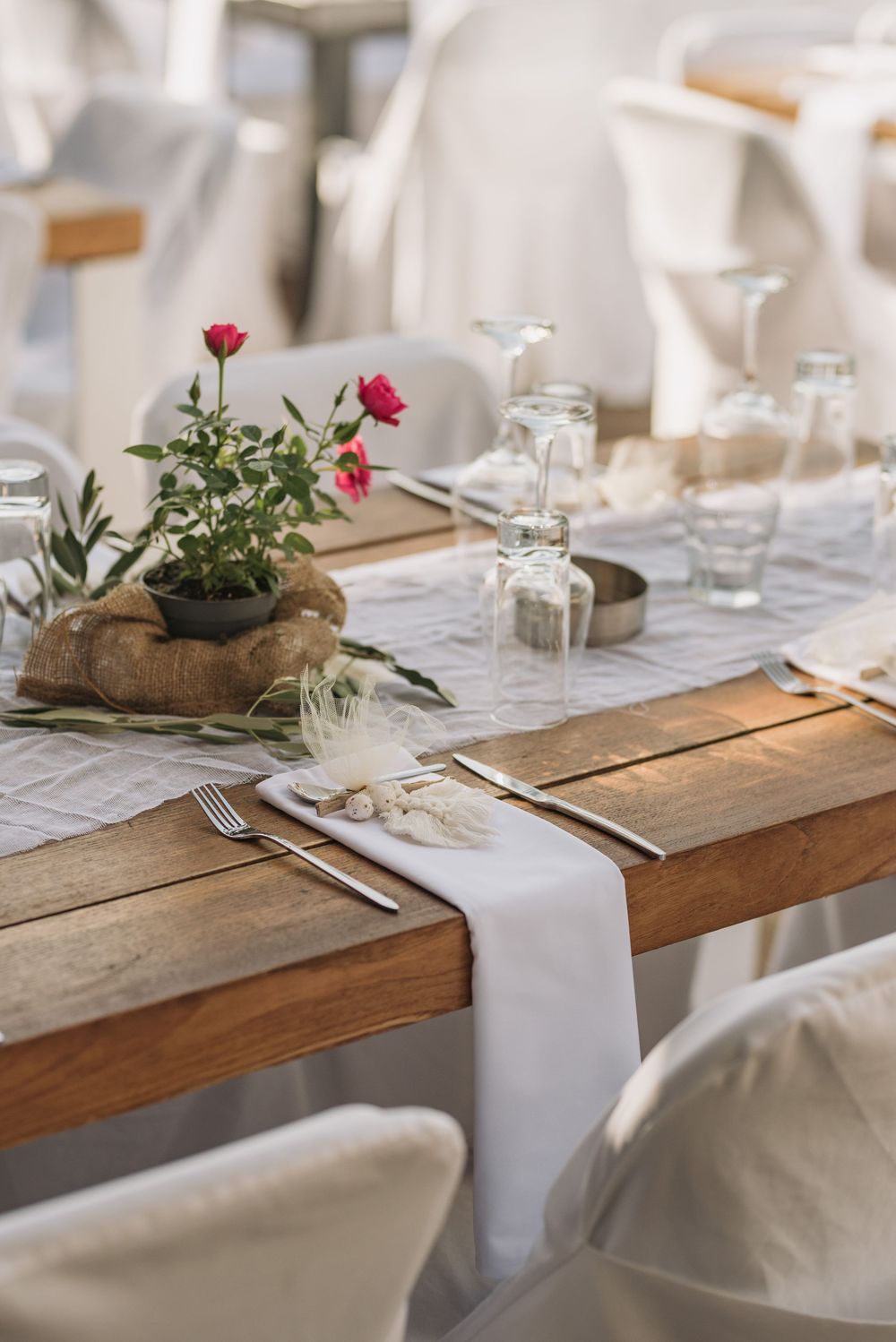Elegant table setting with white runner, pink roses in burlap, and rustic wooden tables for a romantic wedding reception.