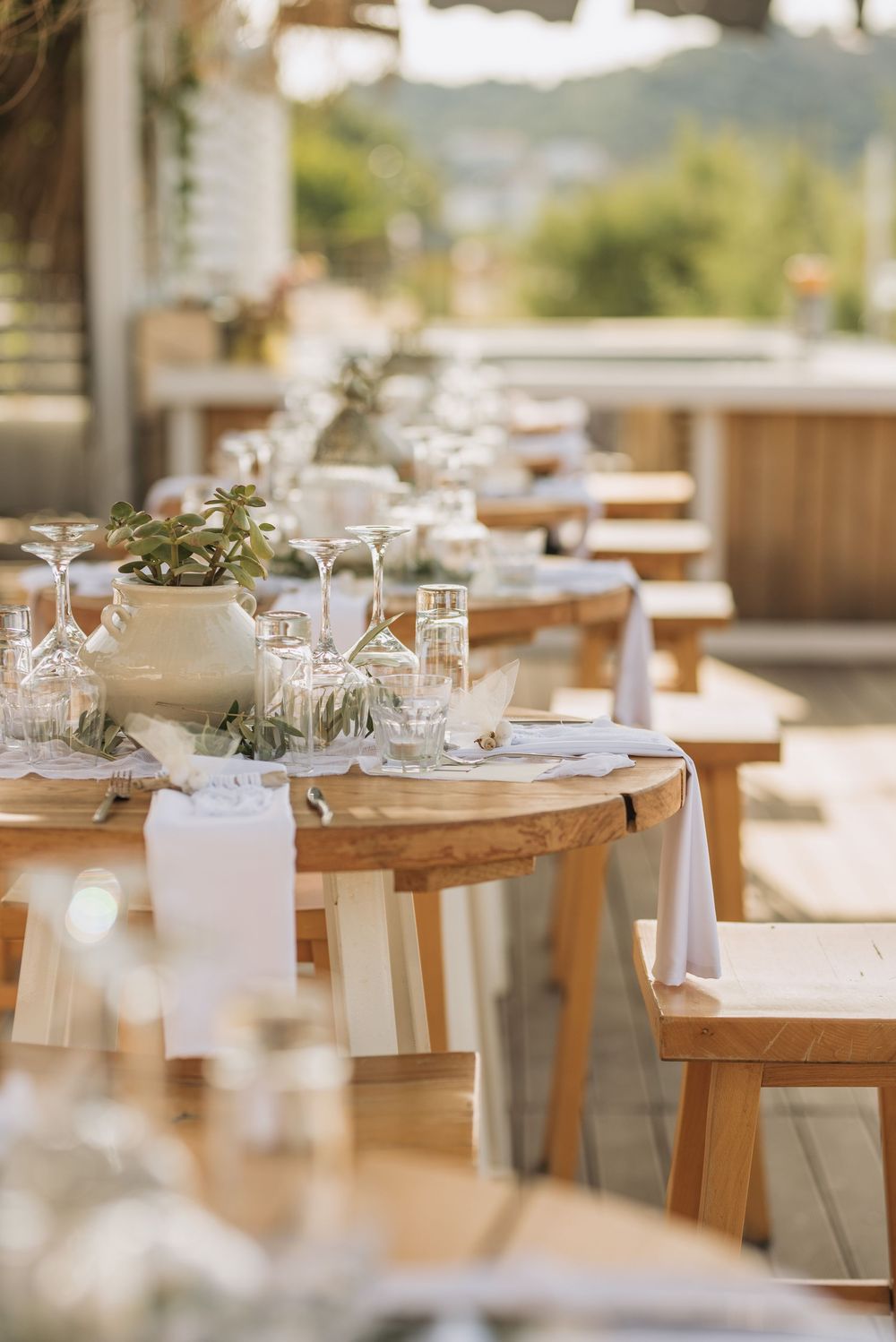 Elegant outdoor wedding reception table setup with wooden furniture, white linens, and delicate glassware.