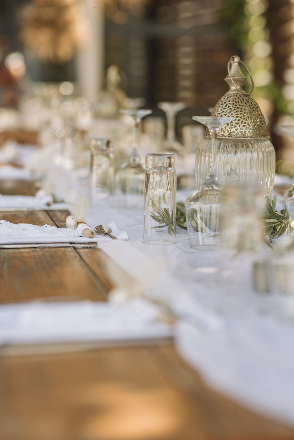 Close-up of wedding table decorations featuring ornate lanterns and glass vessels on white tablecloth.