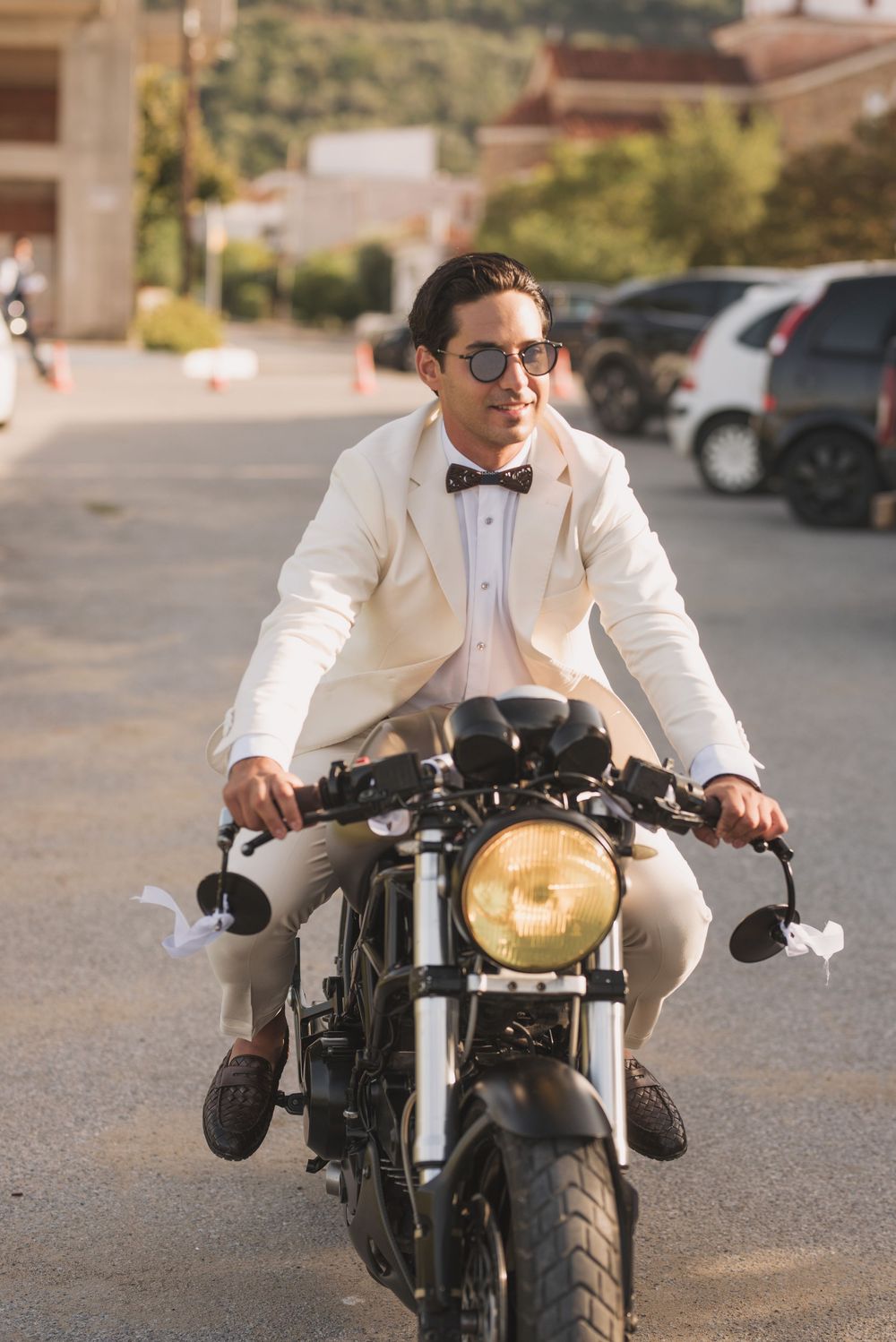 Stylish motorcyclist in white formal suit and bowtie riding vintage cafe racer motorcycle.
