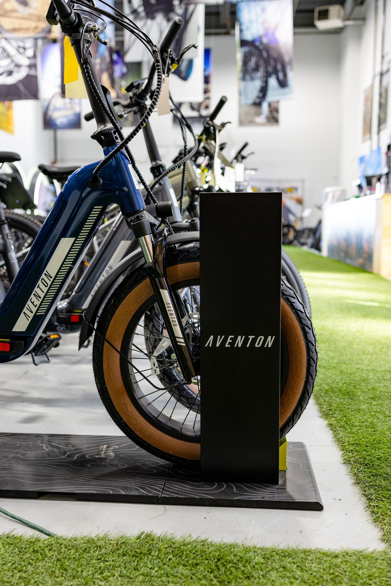 Electric bicycle with Aventon branding displayed on artificial turf in a retail showroom.
