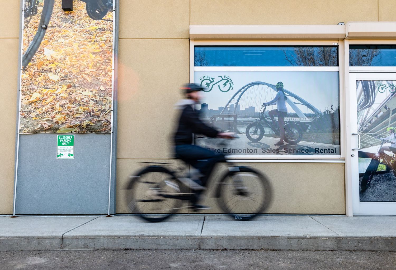 Silhouettes of cyclists in motion against a beige wall with windows.