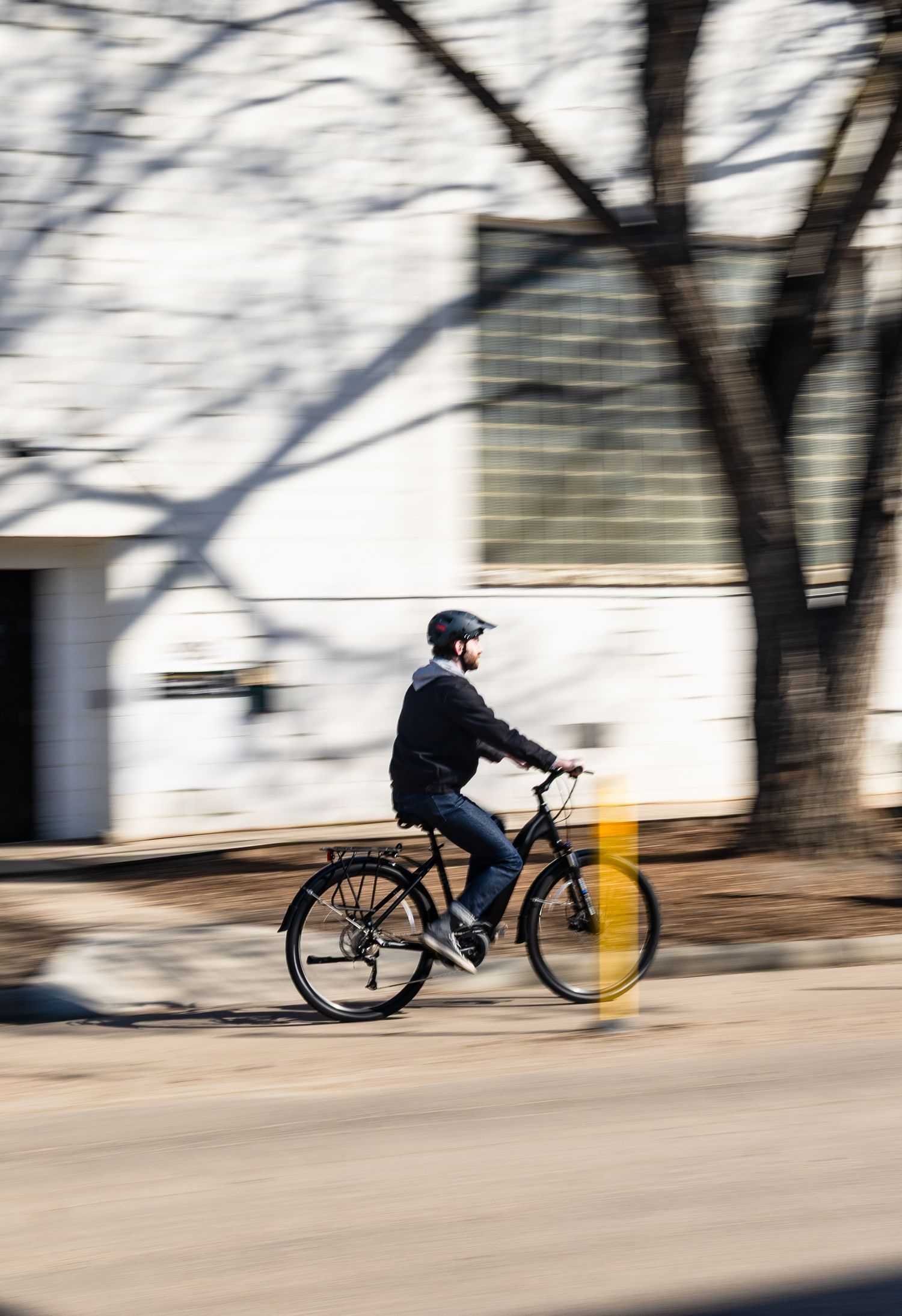 Motion-blurred sequence of cyclist riding an electric bike past trees and shadows.