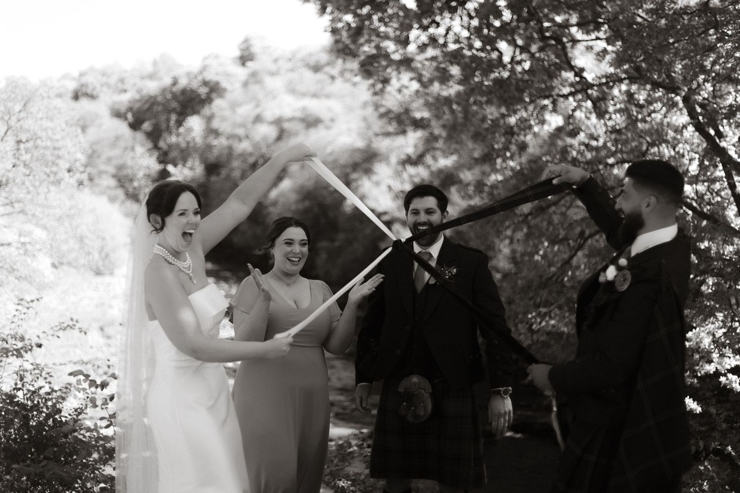 A couple performs a unity ceremony outdoors surrounded by wedding party members during a traditional celebration.