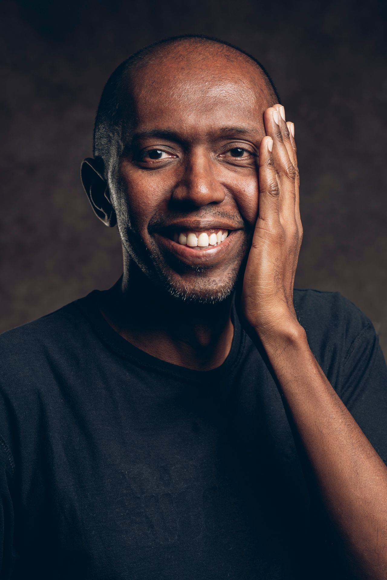 Portrait of a smiling person in a black shirt with hand touching their face.
