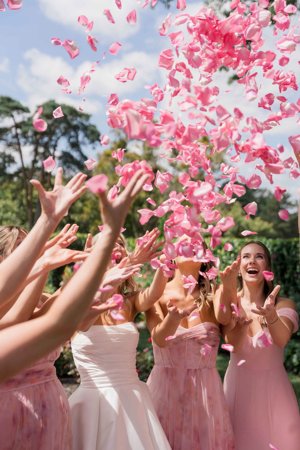 Pink flower petals being tossed in the air at an outdoor wedding celebration.