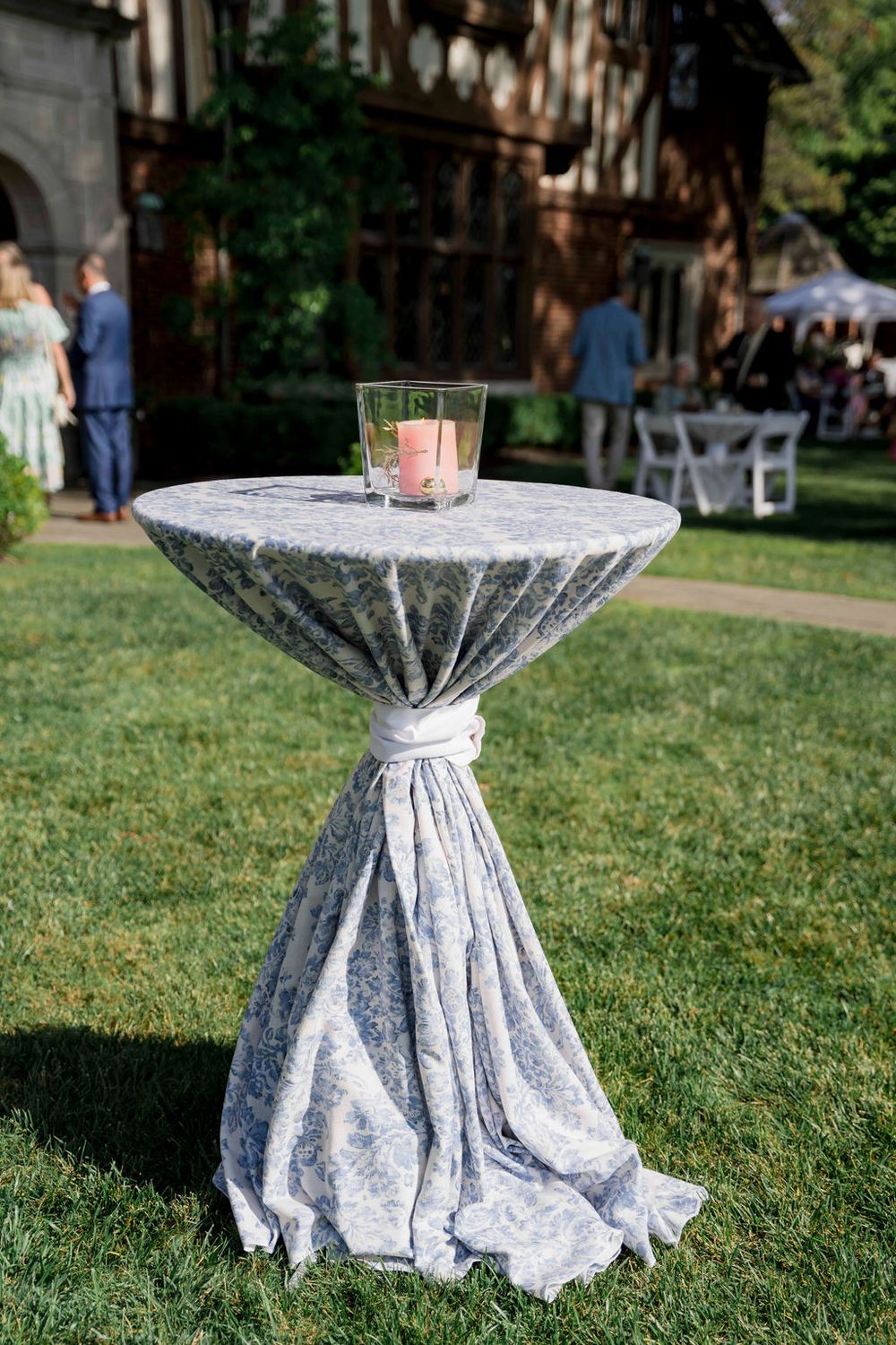 Cocktail table with gray linen tablecloth and pink candle centerpiece at outdoor wedding reception.