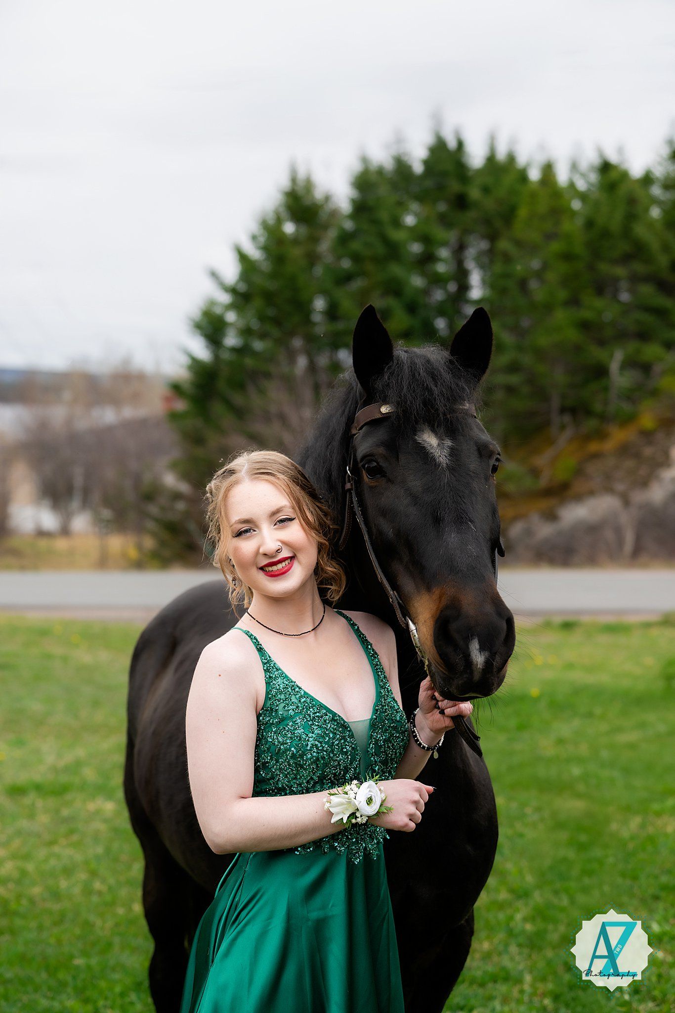 A beautiful black horse poses with someone wearing an emerald green formal gown in a grassy field.