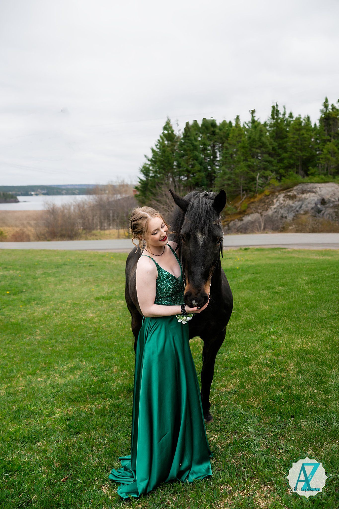 Black horse and someone in sparkly green gown stand together against scenic autumn landscape.