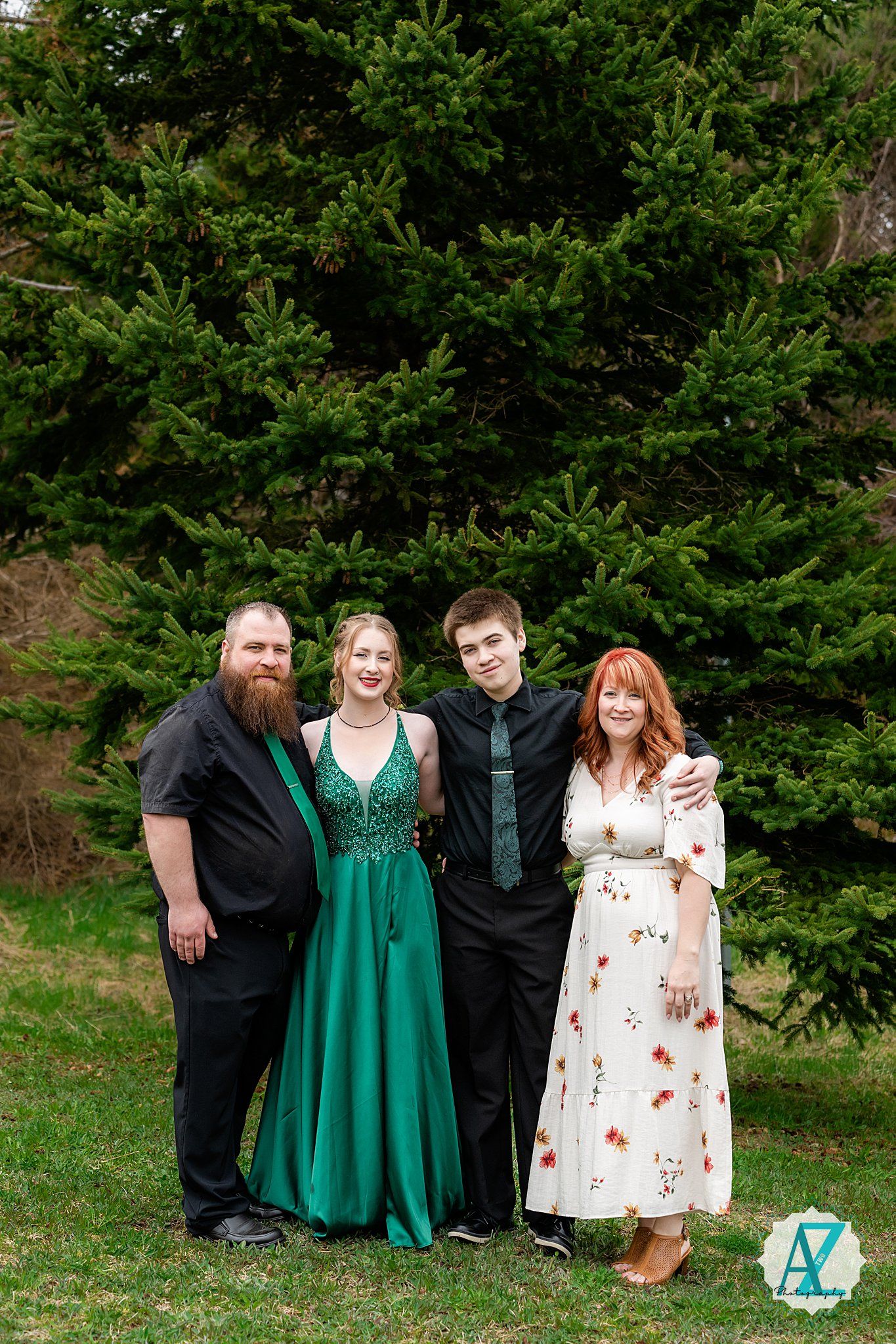 Group photo of four people standing together in front of evergreen trees.