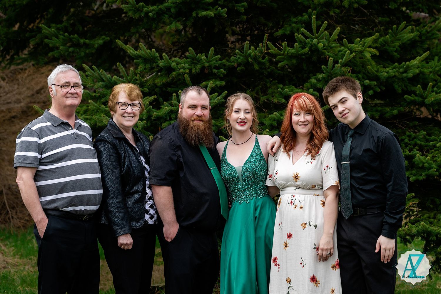 Group of friends and family gather outdoors for a casual portrait against green foliage background.