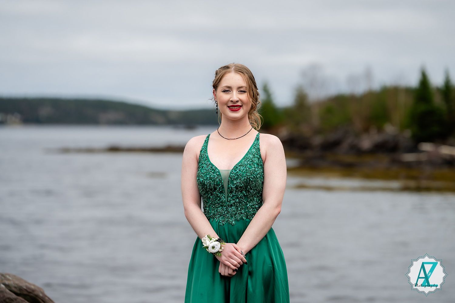 Person stands outdoors by scenic waterfront view wearing an elegant emerald green formal dress.