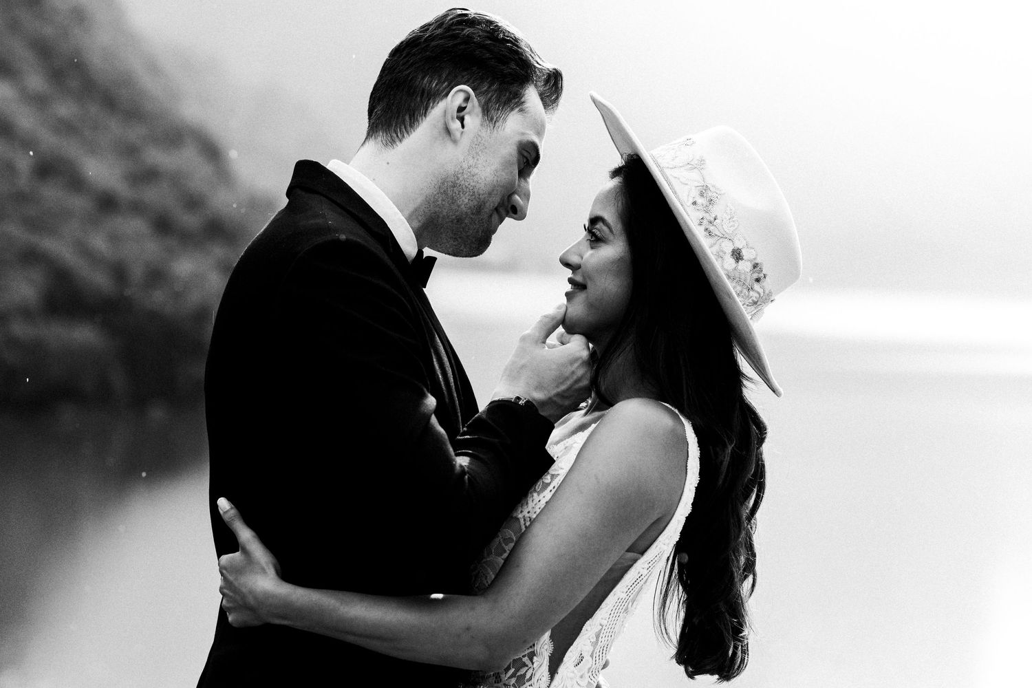 A couple shares an intimate black and white moment on their wedding day against a scenic mountainous backdrop.
