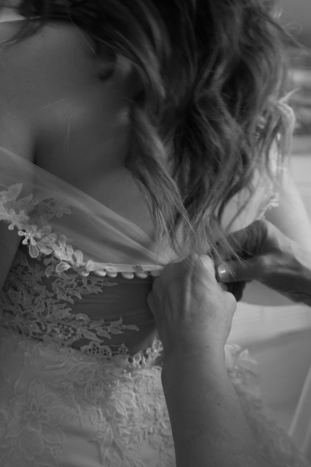 Black and white closeup of intricate lace and beading details being adjusted on a wedding dress.