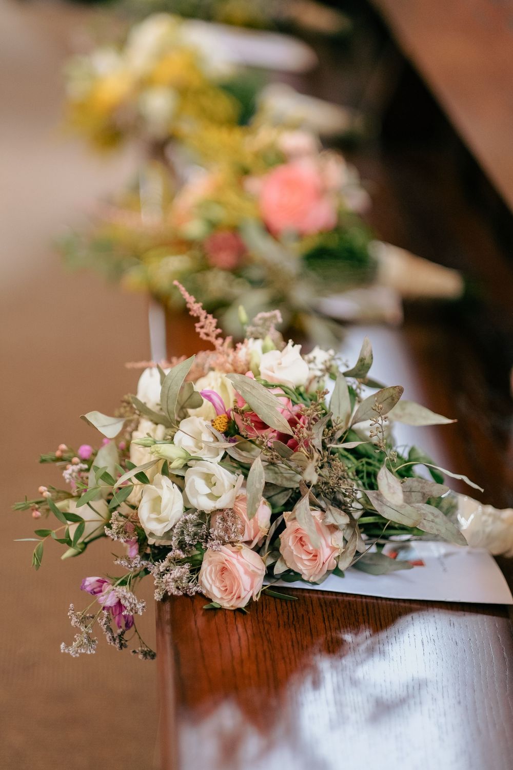 Elegant floral centerpiece with pink roses and white flowers arranged in a wooden vessel on a dark surface.
