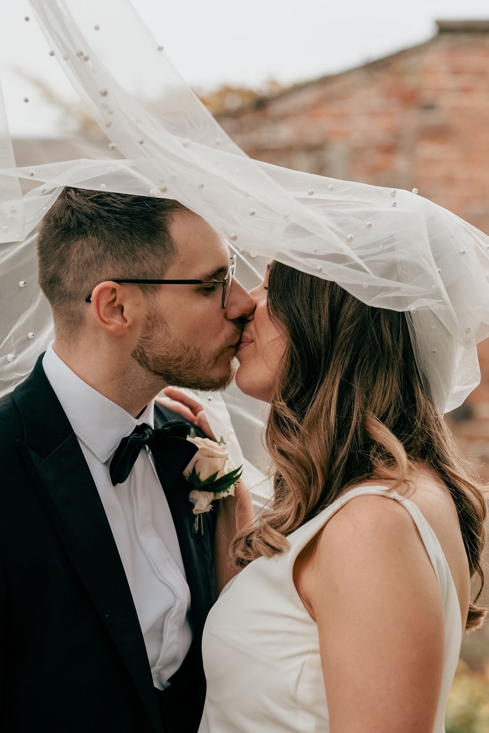 A romantic wedding moment captured as a couple shares a tender kiss under a flowing white veil.