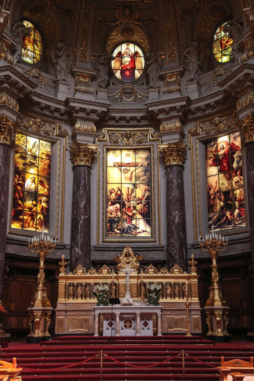 Ornate cathedral interior with stained glass windows, marble columns and golden candelabras around an elaborate altar.