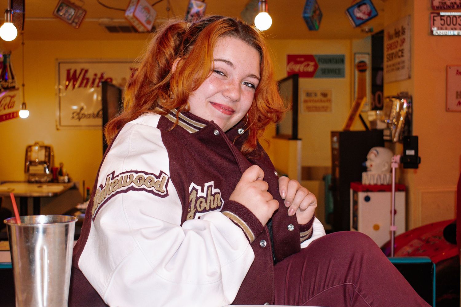 Indoor senior photo of high school girl in letterman jacket with vibrant backdrop in Federal Way, WA. Seattle senior photography