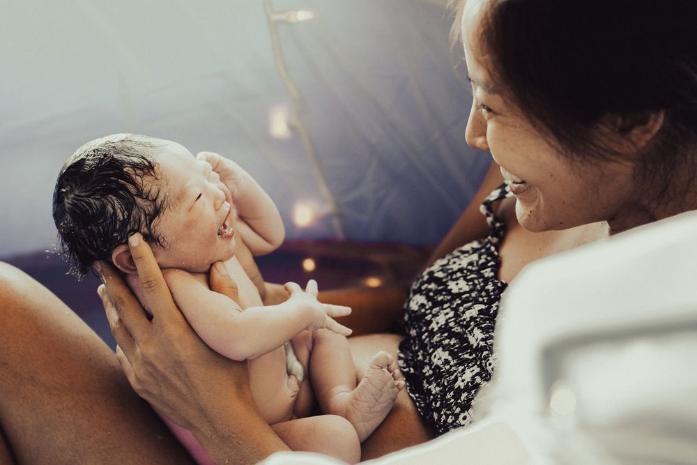 A newborn baby rests peacefully in cradled arms while being admired in warm glowing light. Oahu Newborn Photographer