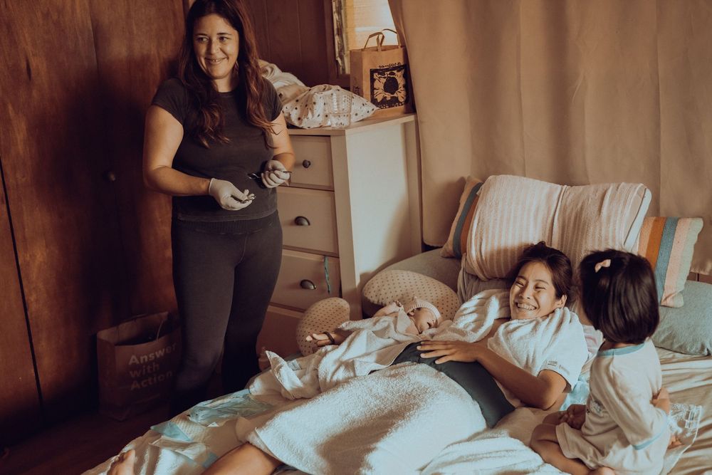 A warm family moment captured in a bedroom as people relax and share stories together in soft lighting. Oahu Newborn Photographer