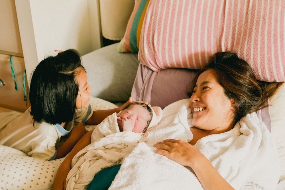 Family enjoying a joyful moment together while relaxing and laughing on a cozy bed at home. Oahu Newborn Photographer