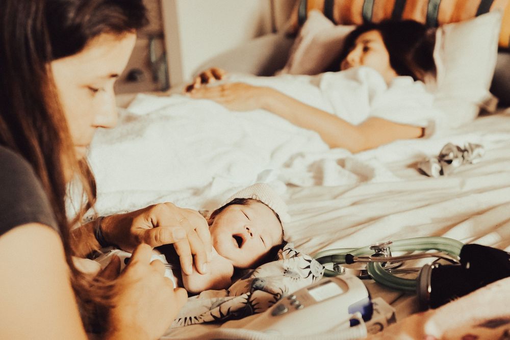A mother and baby share an intimate bonding moment together on white bedding in warm, natural light. Oahu Newborn Photographer