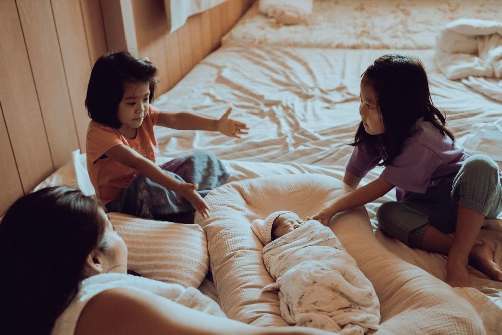 Young people enjoying a casual conversation while relaxing on a cozy bed with white bedding. Oahu Newborn Photographer