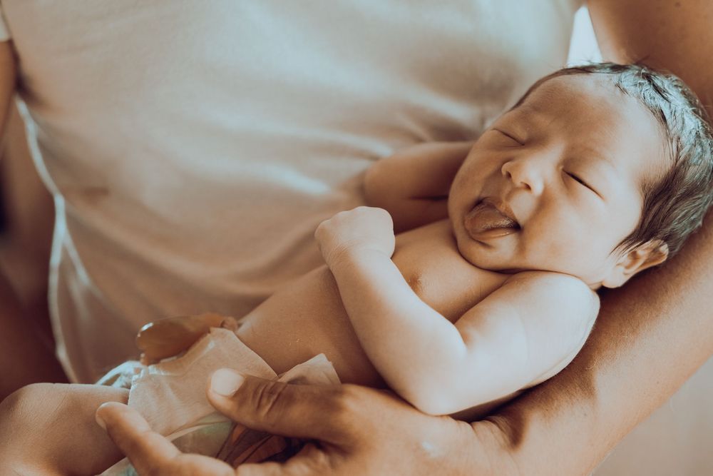 A newborn baby wearing a diaper rests peacefully on white bedding with a gentle smile.　Oahu Newborn　Photographer
