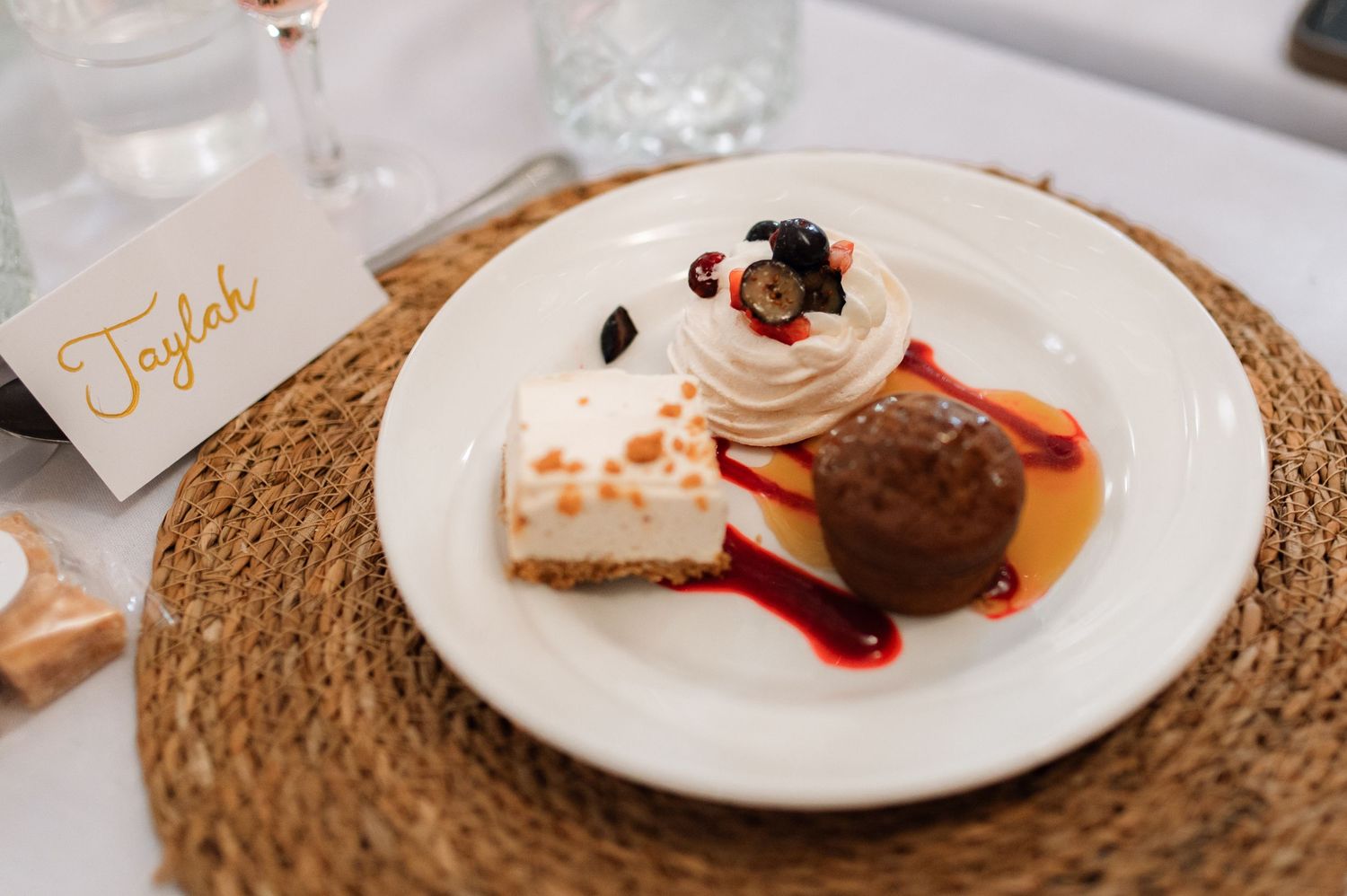 Elegant dessert plate featuring cheesecake, chocolate cake, and whipped cream garnish on a white plate with woven placemat.