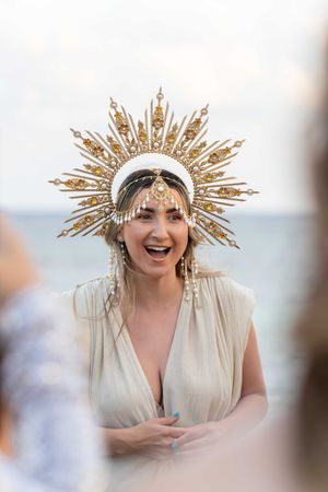 Woman wearing ornate golden sunburst crown headpiece smiles during celebration.