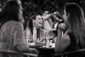 Black and white candid photo of people enjoying conversation at a dimly lit dinner gathering.