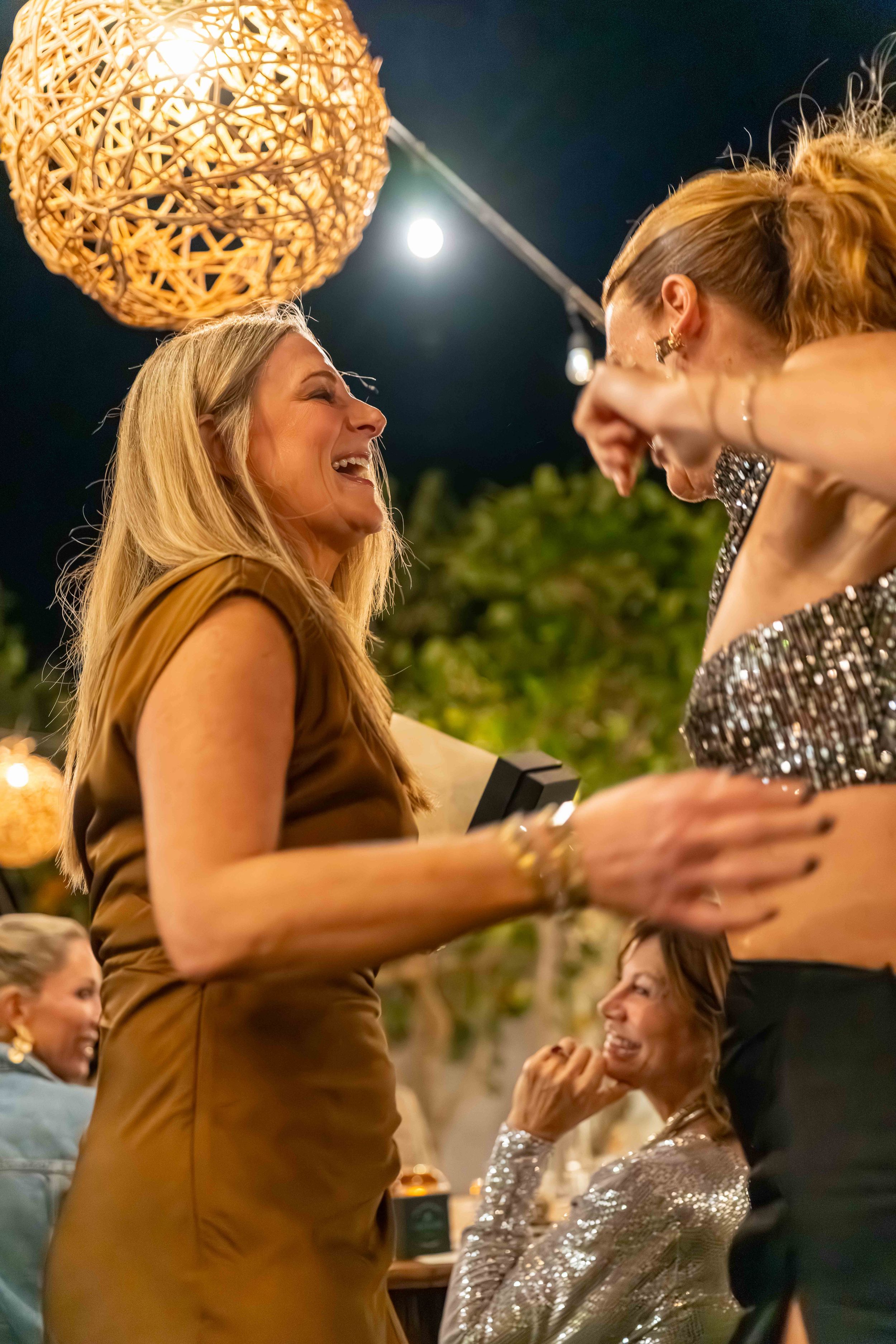 Joyful celebration under warm lighting with decorative woven orb lamp overhead.
