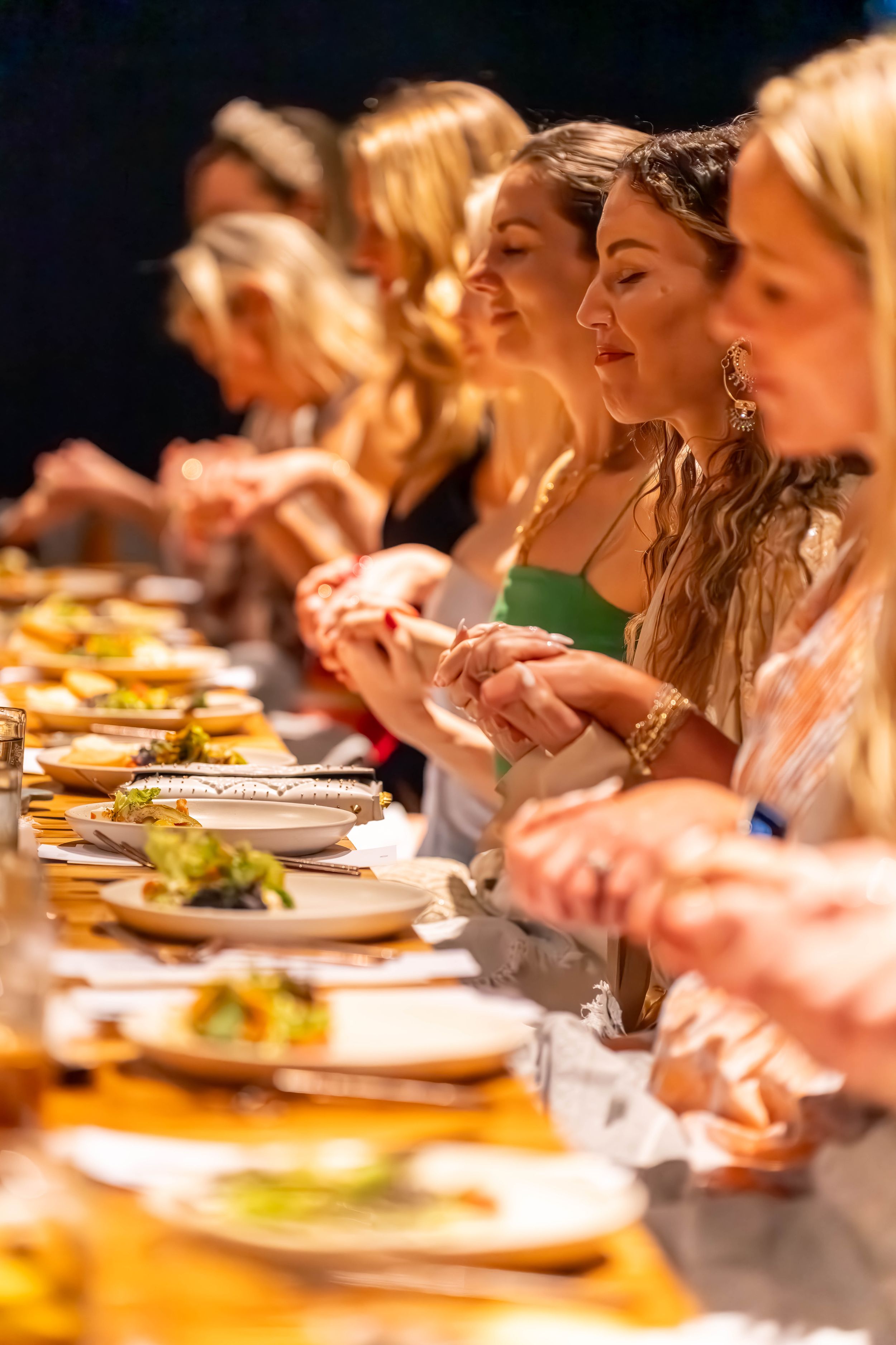 A line of people enjoying a communal dining experience at a long table filled with colorful plates of food.