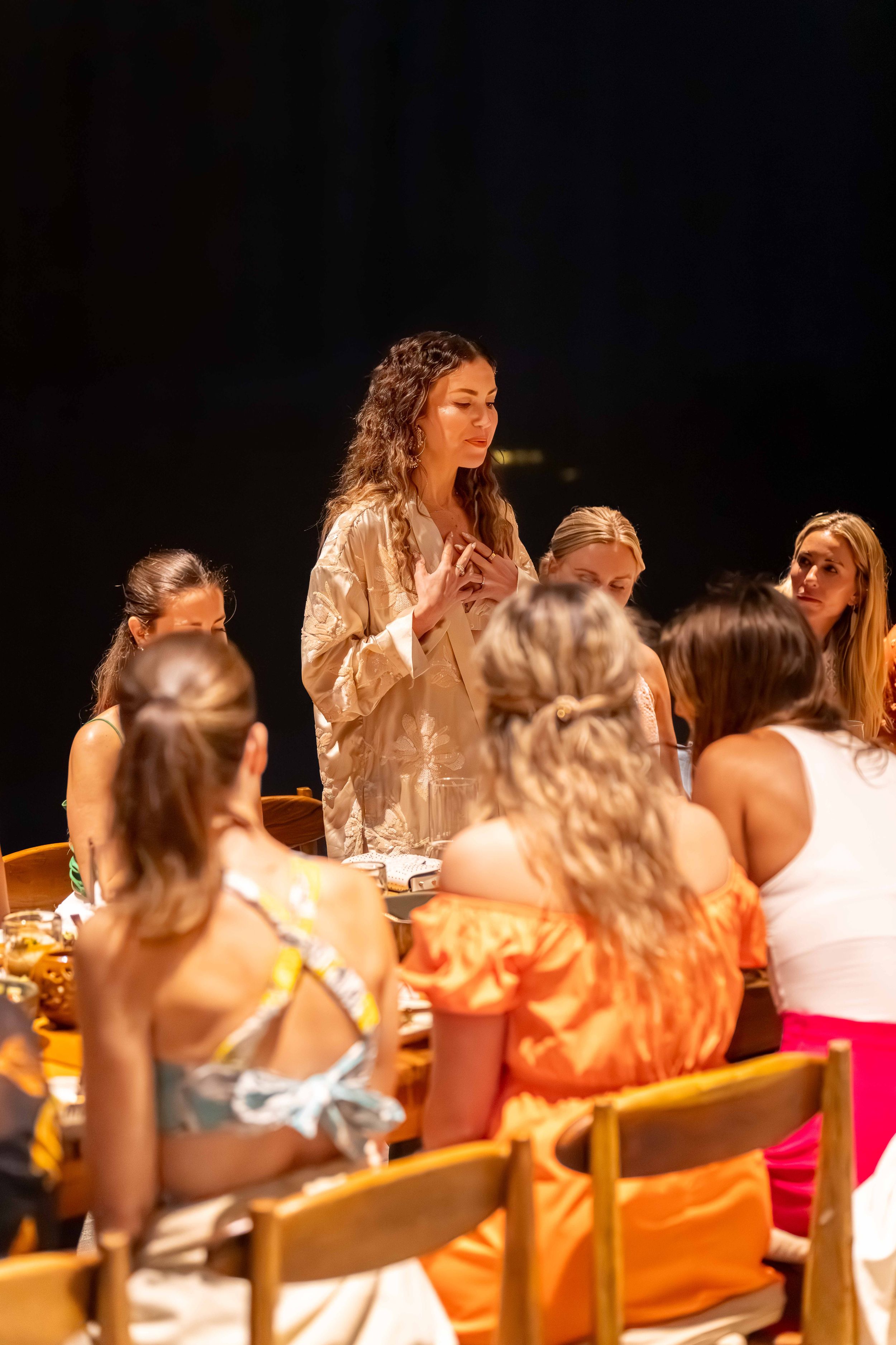 A gathering of people at an evening event with someone speaking to the seated group.