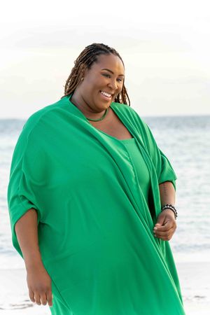 Person in vibrant green dress smiling joyfully on beach during sunset.