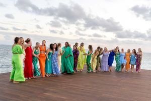 Line of people in bright colored dresses posing together on wooden pier over ocean.