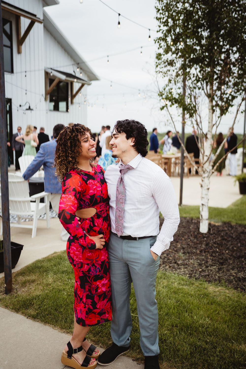 A couple in formal attire share a romantic moment outside a white barn venue during a wedding celebration.