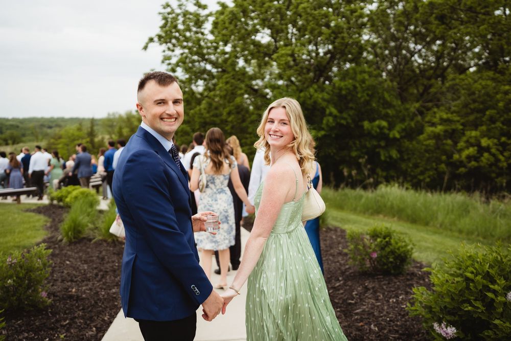 People at an outdoor event enjoy a sunny day on landscaped grounds with trees in the background.